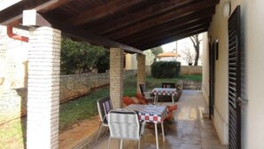Un patio cubierto con mesa y sillas, un muro de ladrillo y vistas a un jardín.