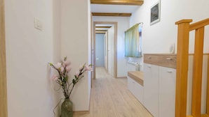 A narrow hallway with wooden flooring, white walls, and a wooden staircase on the right. A vase with flowers is placed on the left side. - Holiday home with air conditioning (Vodnjan)