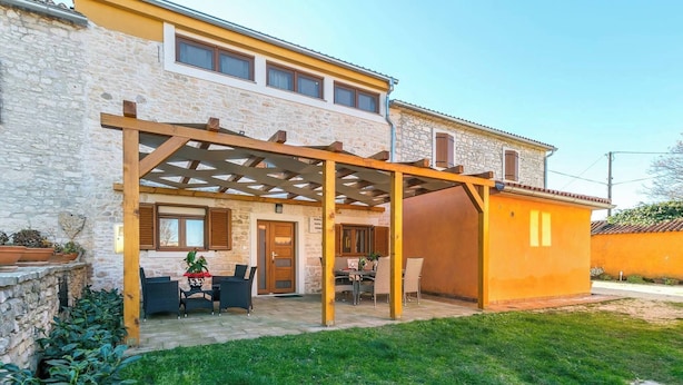A two-story house with a stone facade, a wooden pergola, and a small patio area with outdoor furniture. - Holiday home with air conditioning (Vodnjan)