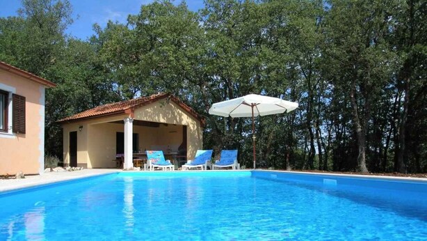 Una piscina con sillas de descanso y un pequeño edificio de techo con tejas.