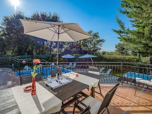 Une terrasse extérieure avec une table dressée pour le repas, entourée de chaises et d’un grand parasol.