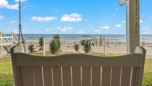 A beach view from a porch with a swing, palm trees, and a golf cart. - Laid-Back Beachfront Bungalow (Galveston)