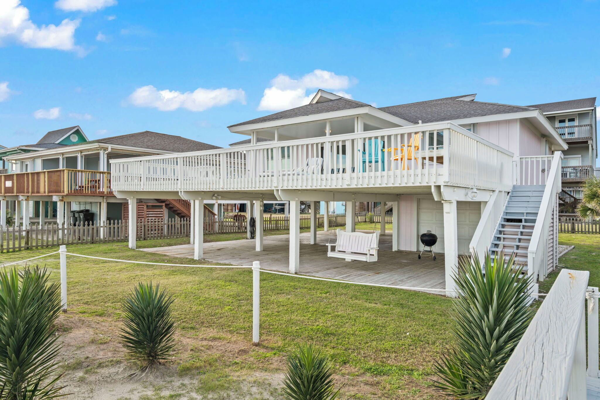 Une maison située en bord de mer, dotée d’une terrasse couverte, d’un espace barbecue et d’un escalier menant à un deuxième étage.