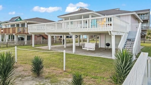 A beachfront house with a covered deck, a barbecue area, and a staircase leading to a second floor. - Laid-Back Beachfront Bungalow (Galveston)