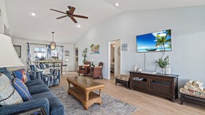 A spacious living room with a large sofa, a coffee table, and a television mounted on the wall. - Laid-Back Beachfront Bungalow (Galveston)