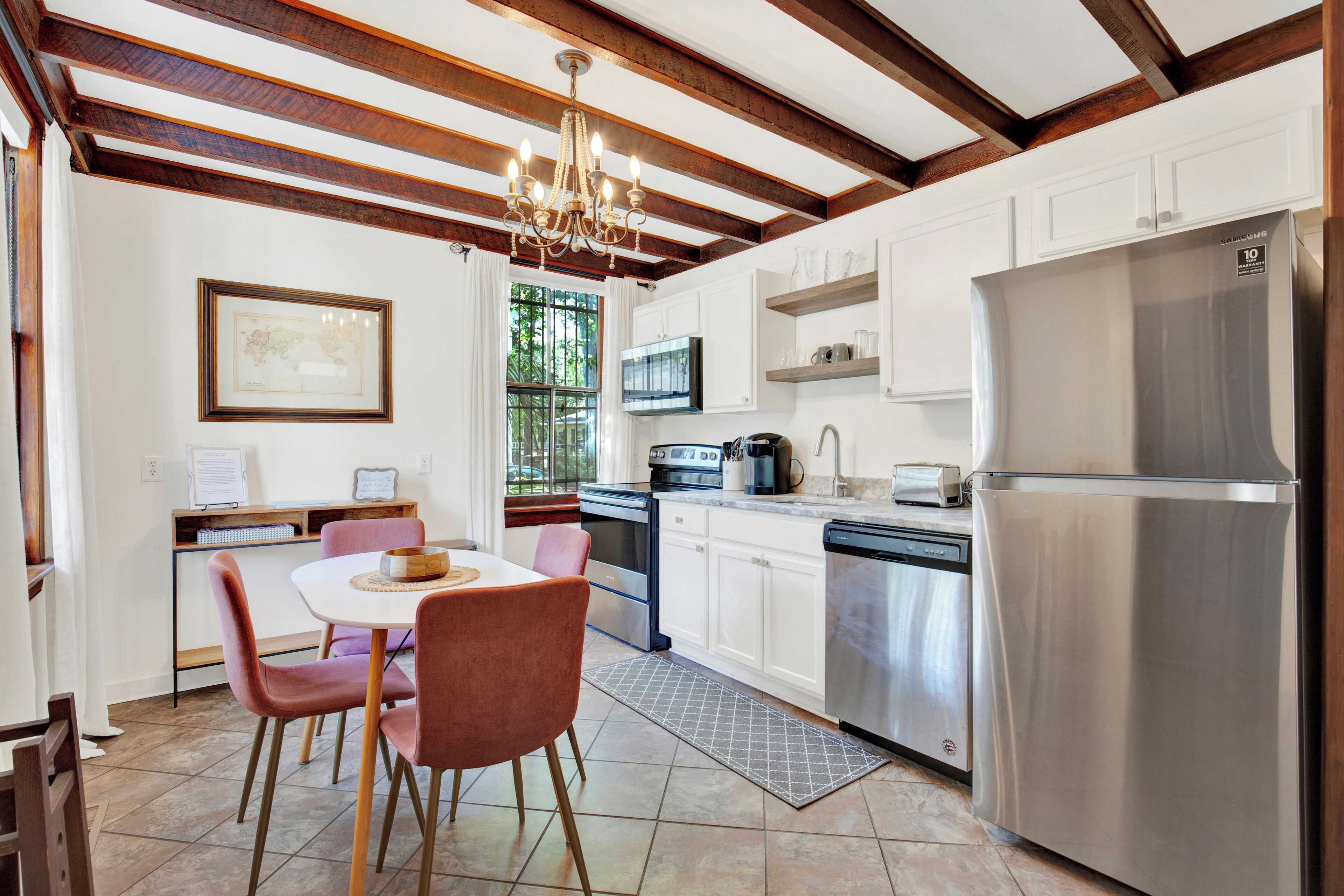 A modern kitchen with white cabinets, a stainless steel refrigerator, and a dining area with pink chairs.