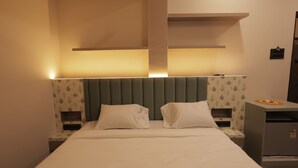Une chambre d’hôtel comprenant un lit, deux tables de chevet, une petite table, une commode et une étagère fixée au mur.