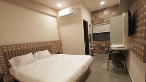 Ein Hotelzimmer mit Bett, Schreibtisch, Stuhl, Klimaanlage und Fernseher.