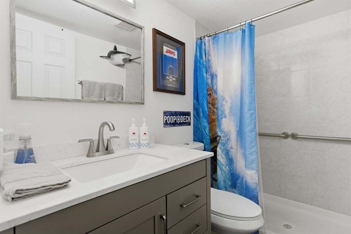A bathroom with a white sink, a mirror, a toilet, and a shower curtain with a cat design.