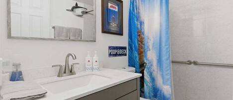 A bathroom with a white sink, a mirror, a toilet, and a shower curtain with a cat design.