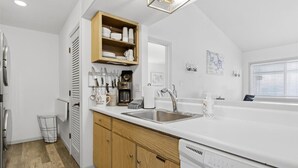 Een moderne keuken met witte kastjes, een inbouwoven, een vaatwasser en een aanrecht met diverse apparaten.