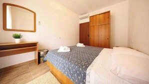 Un dormitorio con cama, un armario de madera, una mesita de noche con una planta y un espejo en la pared.