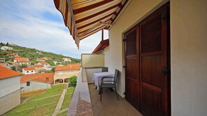 Un balcón con mesa y sillas, vista a una colina con casas y una puerta de madera.