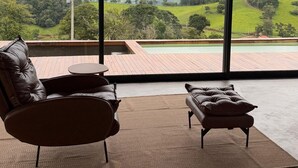 A spacious room with a large window offering a view of a green landscape. There is a leather sofa and a small table. - Casa c Piscina e Vista Panor Mica Bueno Brand o (Pouso Alegre)