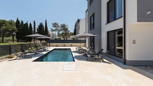 A modern building with a swimming pool, sun loungers, and umbrellas. - Holiday apartment with air conditioning and shared pool (Funtana)