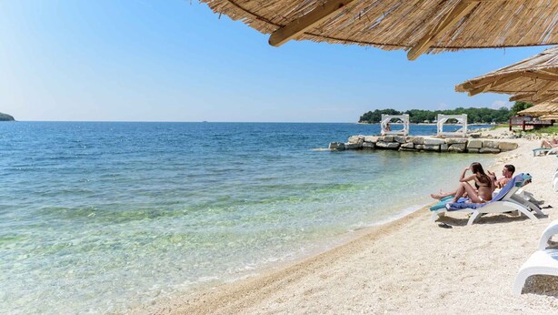 A beach with clear water, a thatched roof structure, and a small pier. - Holiday apartment with air conditioning and shared pool (Funtana)