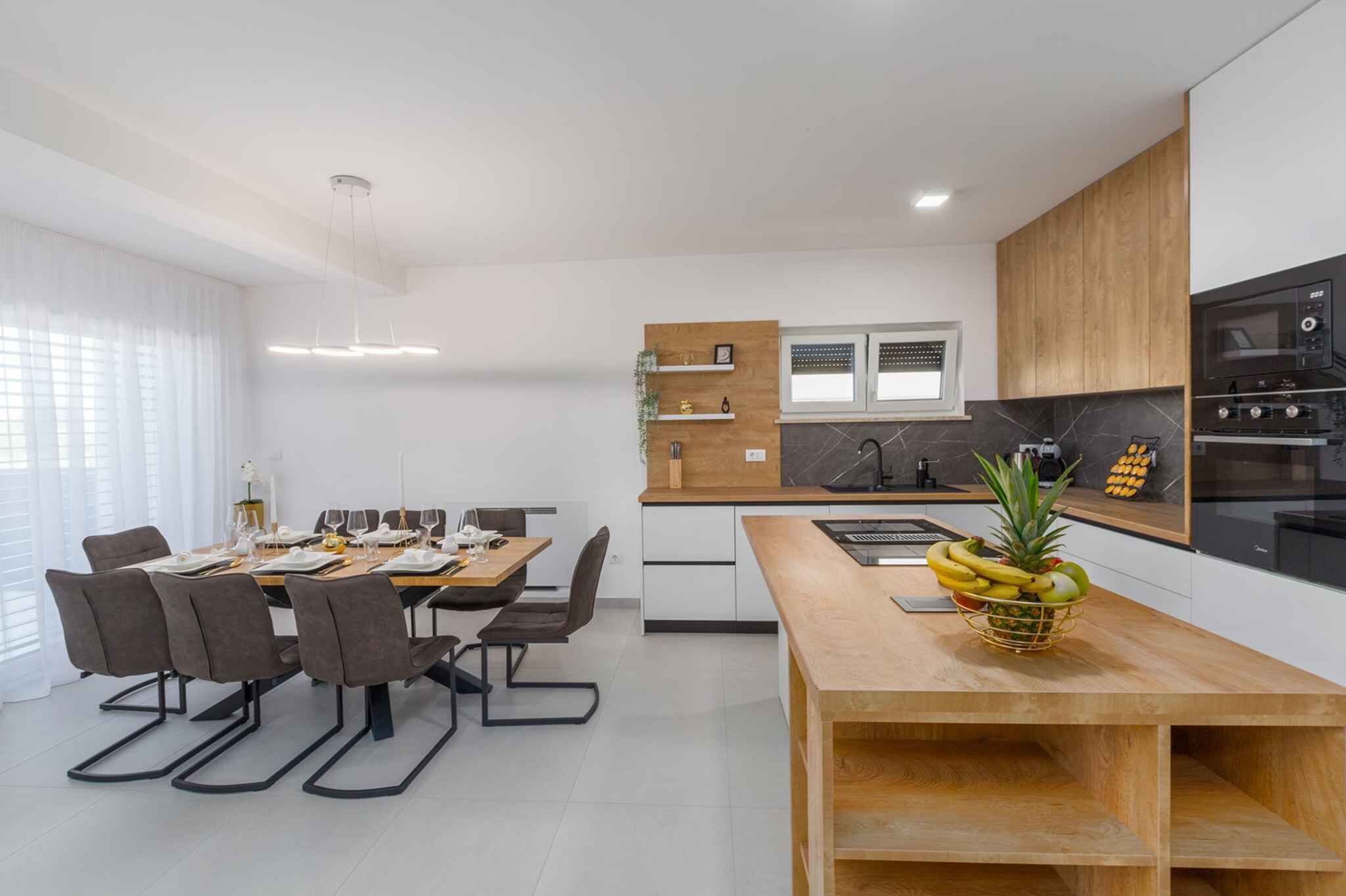 Une cuisine moderne avec des meubles en bois, un four encastré et un coin repas comprenant une table et des chaises en bois.