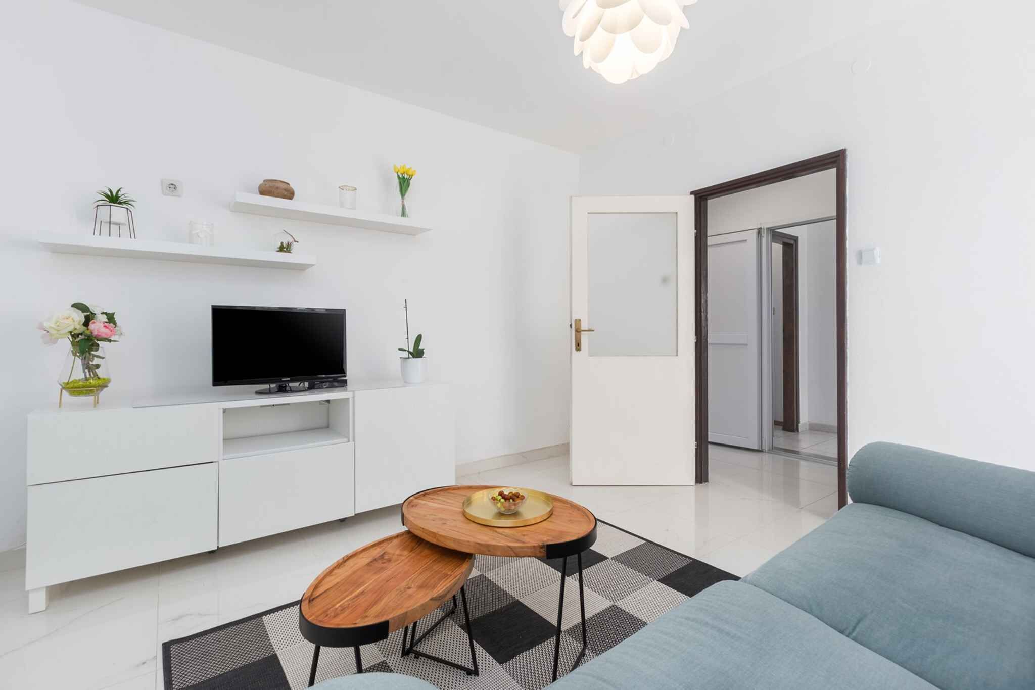 A modern living room with a flat-screen TV, white cabinetry, a sofa, and a dining area with two tables.