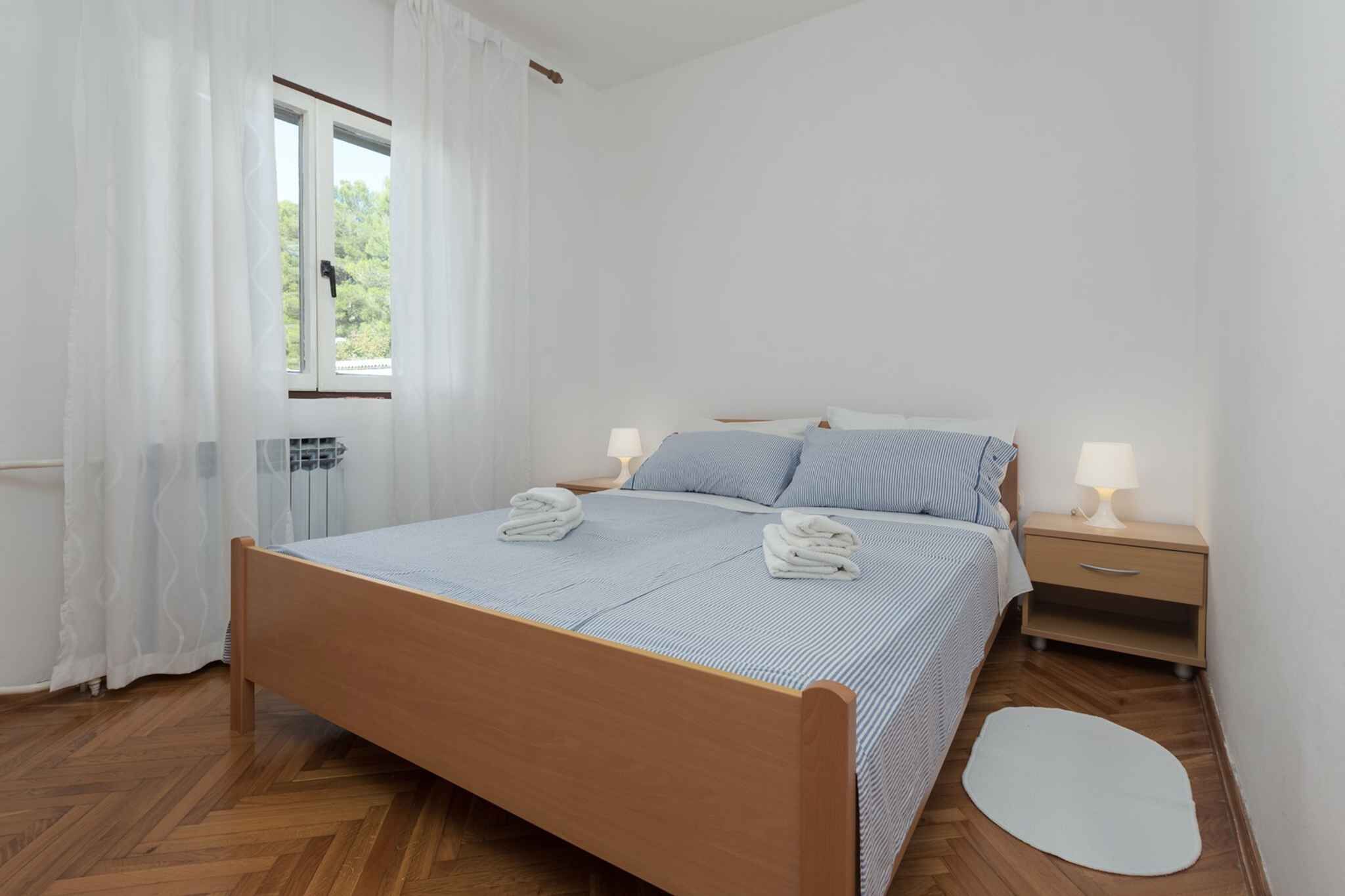 Um quarto com cama de madeira, duas mesas de cabeceira com abajures, uma janela com cortinas e um tapete branco.