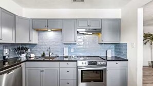 Una cucina moderna con mobili grigi, piano cottura in acciaio inossidabile e zoccolo in piastrelle.