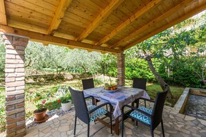 Eine überdachte Terrasse mit Tisch und Stühlen, umgeben von Kübelpflanzen und einer Ziegelmauer.