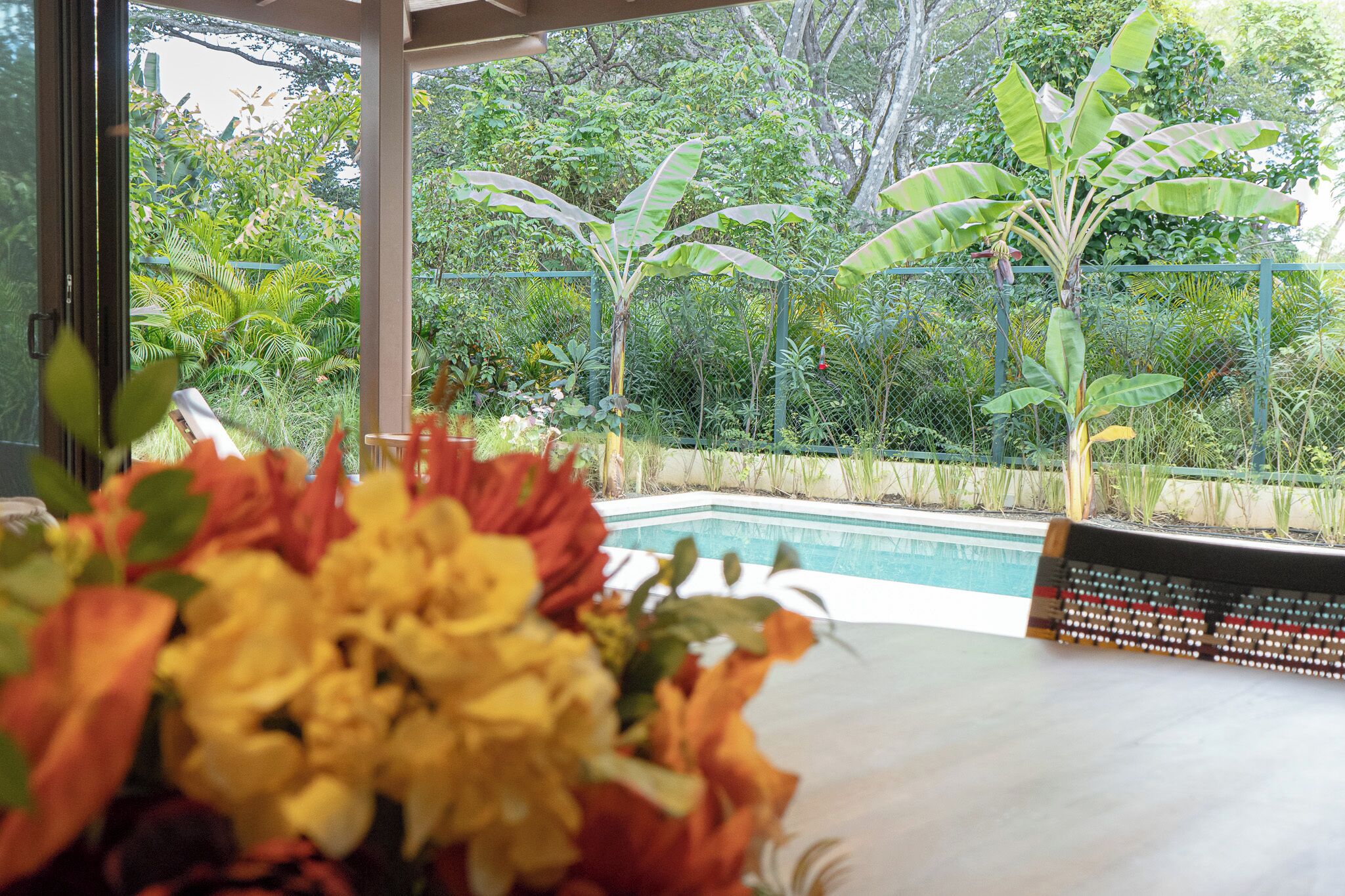 A poolside view with a lush garden and a table with a floral arrangement.