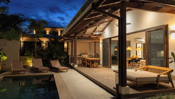 Area piscina esterna moderna con poltroncini, un solarium in legno e una zona pranzo con tavolo e sedie.