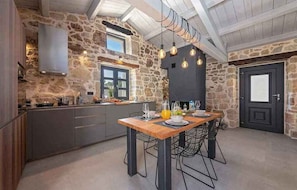 Une cuisine rustique avec des murs en pierre, une table à manger en bois et des luminaires suspendus.