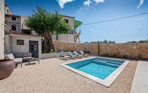 Une piscine avec des chaises longues, un mur en pierre et un arbre.
