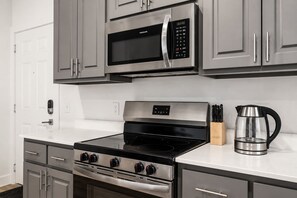Une cuisine équipée d’un four à micro-ondes en acier inoxydable, d’une cuisinière à quatre brûleurs et d’une machine à café.
