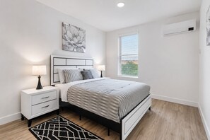Une chambre moderne comprenant un lit, des tables de chevet, une commode, une fenêtre avec stores et un appareil de climatisation.