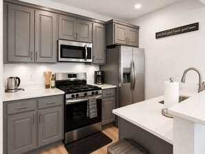 A modern kitchen with grey cabinets, stainless steel appliances, a microwave, stove, refrigerator, and a sink with a faucet. - Modern Luxury Suite • Downtown Hot Springs (Hot Springs)