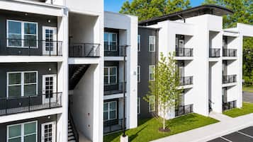 A modern multi-story residential building with balconies, a central staircase, and a small tree in the front yard.