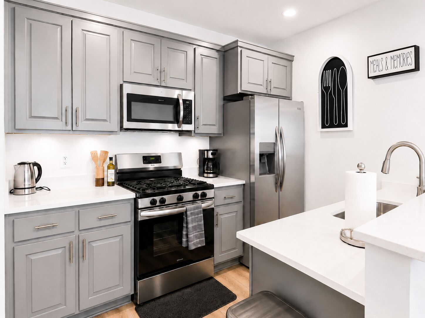 A modern kitchen with grey cabinets, a stainless steel refrigerator, a microwave, a stove, and a coffee maker.