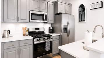 A modern kitchen with grey cabinets, a stainless steel refrigerator, a microwave, a stove, and a coffee maker.