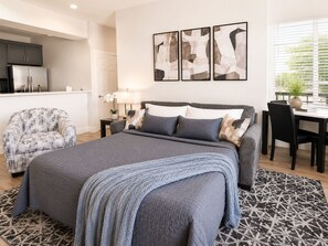 A modern bedroom with a large bed, a sofa, a dining table, and a kitchen area. - Modern Luxury Suite • Downtown Hot Springs (Hot Springs)
