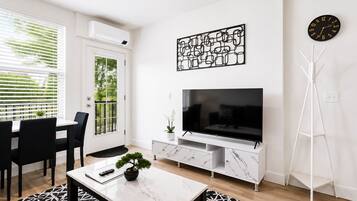 A modern living room with a TV, a dining area with chairs, a white console table, and a floor lamp.