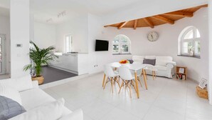 Een ruime woonkamer met een eettafel, witte banken en een keuken op de achtergrond.