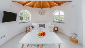 Een ruime kamer met een witte tafel, een witte bank en een houten plafond.