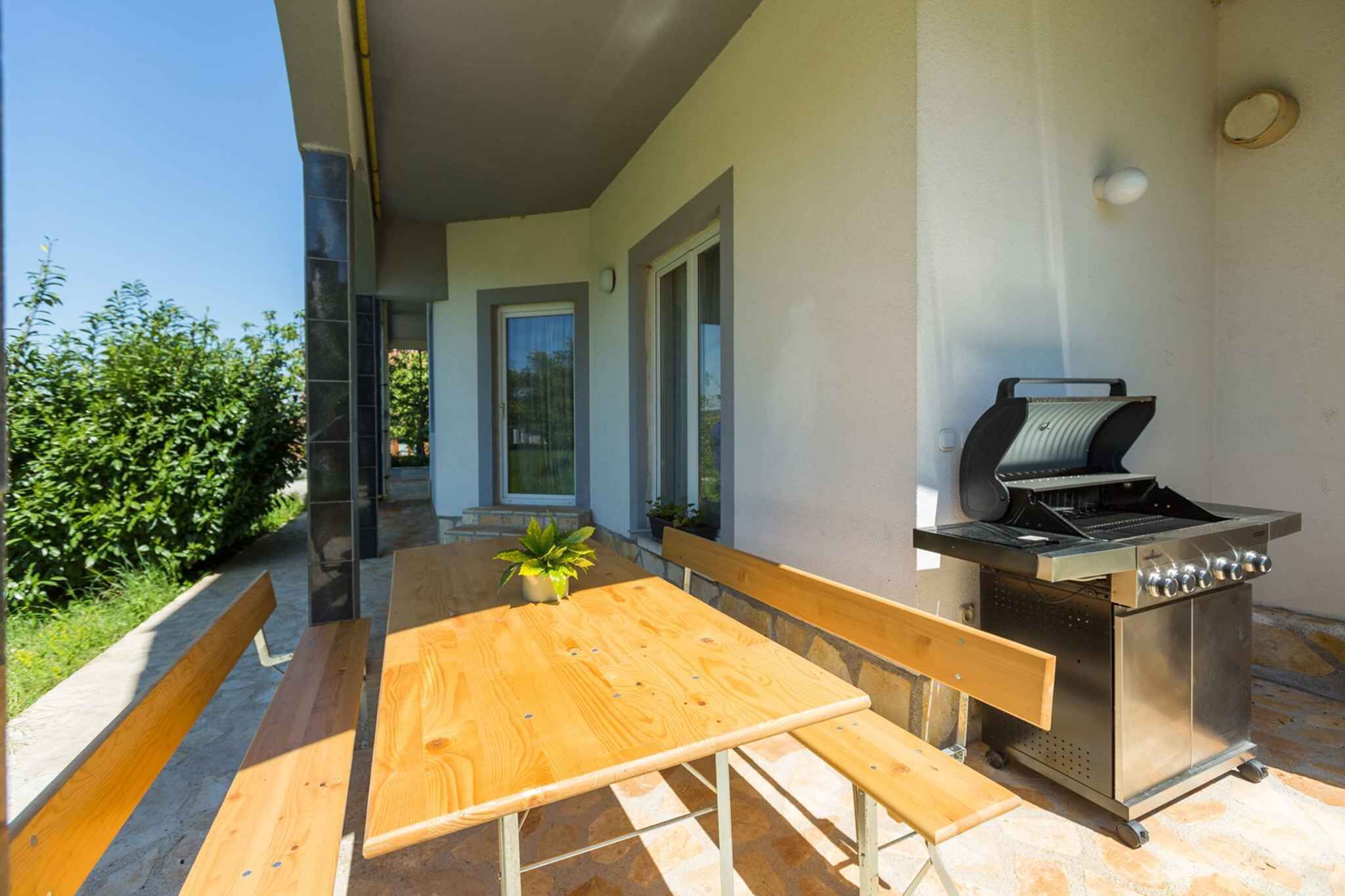 Eine Außenpatio mit einem Holztisch und Bänken, einem Edelstahlgrill und einem Blumentopf.