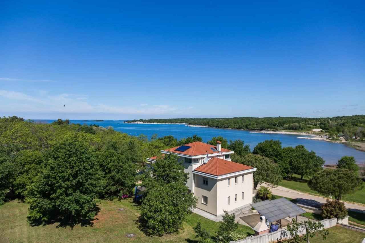 Una casa de dos pisos amb teulada vermella, envoltada de vegetació exuberant i vistes a una gran massa d'aigua.