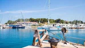 Un puerto deportivo con varios veleros amarrados, una estructura de madera en primer plano y edificios al fondo.