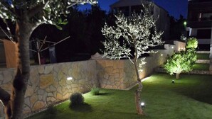A landscaped garden with a stone wall, a well-lit tree, and a small bush. - Holiday apartment with pool and air conditioning (Sv. Filip i Jakov)