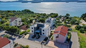 A residential area with modern houses, a parking lot, and a view of a large body of water with mountains in the background. - Holiday apartment with pool and air conditioning (Sv. Filip i Jakov)