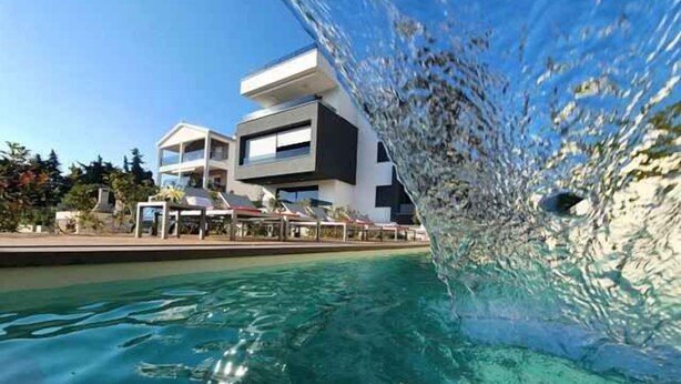 A clear view of a swimming pool with a modern building in the background. - Holiday apartment with pool and air conditioning (Sv. Filip i Jakov)