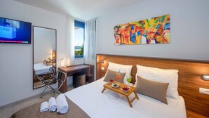 A hotel room with a bed, a desk, a chair, a TV, a painting, and a window with curtains. - Holiday apartment with pool and air conditioning (Sv. Filip i Jakov)