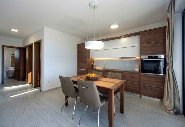 A modern kitchen with wooden cabinets, a built-in oven, and a dining area with a table and chairs.