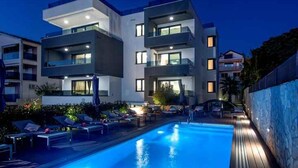 Un edificio moderno con piscina, sillas de descanso y un muro de piedra.