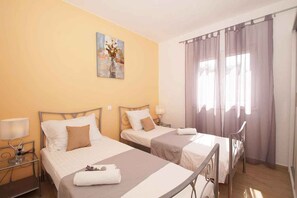 Quarto de hotel com duas camas, um quadro na parede, uma janela com cortinas e uma mesa de cabeceira com abajur.