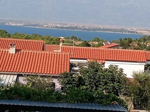 A residential area with red-tiled roofs, a body of water in the background, and greenery in the foreground. - Holiday apartment with barbecue facilities and terrace (Vir)